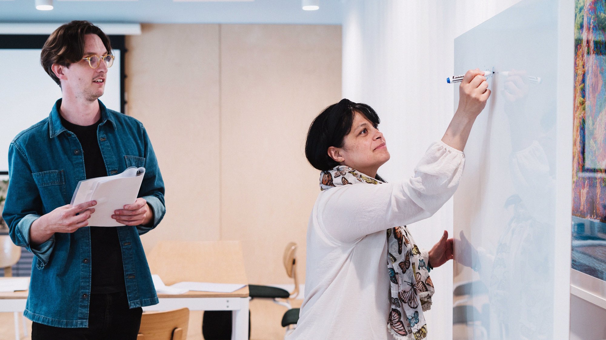 a photo of two Flatiron UK employees brainstorming at a whiteboard a photo of two Flatiron UK employees brainstorming at a whiteboard